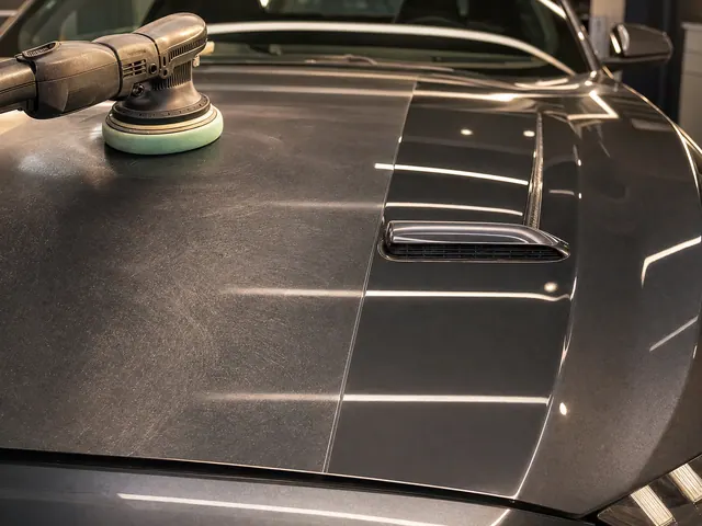 The bonnet of a grey Ford Mustang mid paint correction, a machine polisher on the swirled half beside the half already polished to a mirror.